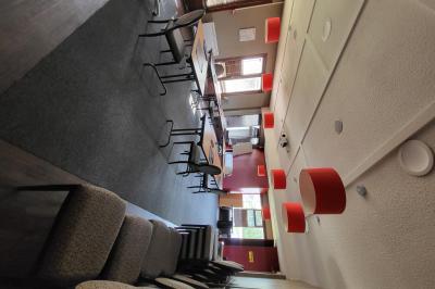 Salle de réunion avec chaises empilées, tables disposées en rangées et luminaires rouges suspendus.