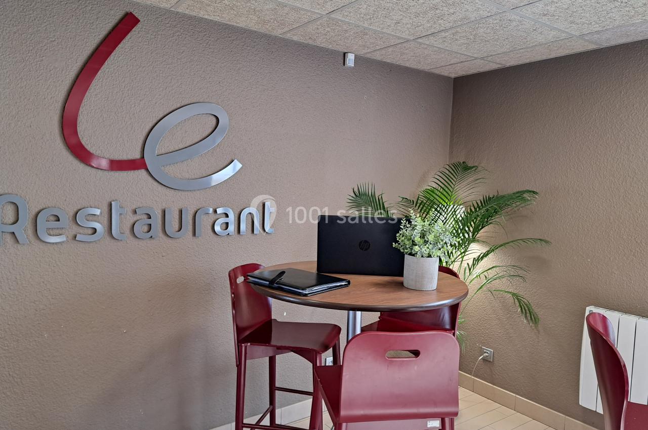 Table haute avec deux chaises rouges, un ordinateur portable et une plante, dans un coin de restaurant avec logo mural.