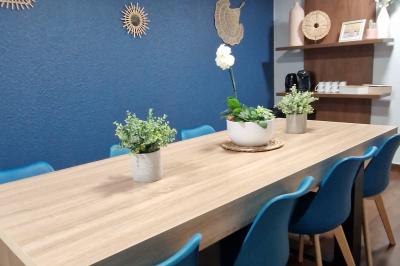 Salle de réunion lumineuse avec table en bois, chaises bleues, écran mural et affichage d'accueil.