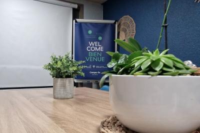 Salle de réunion lumineuse avec table en bois, chaises bleues, écran mural et affichage d'accueil.