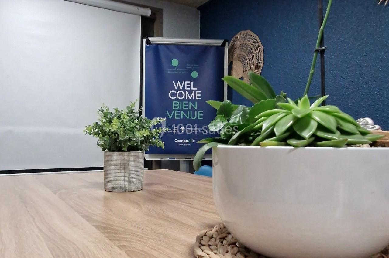 Salle de réunion avec table en bois, plantes décoratives et écran de projection en arrière-plan.