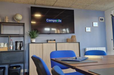 Salle de réunion lumineuse avec table en bois, chaises bleues, écran mural et affichage d'accueil.