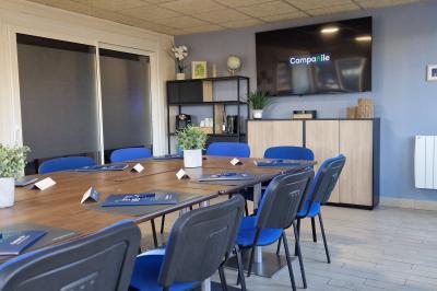 Salle de réunion lumineuse avec table en bois, chaises bleues, écran mural et affichage d'accueil.
