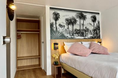 Façade d'un bâtiment à étages avec balcons bleus, partiellement cachée par un arbre sous un ciel nuageux.