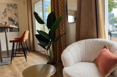 Façade d'un bâtiment à étages avec balcons bleus, partiellement cachée par un arbre sous un ciel nuageux.