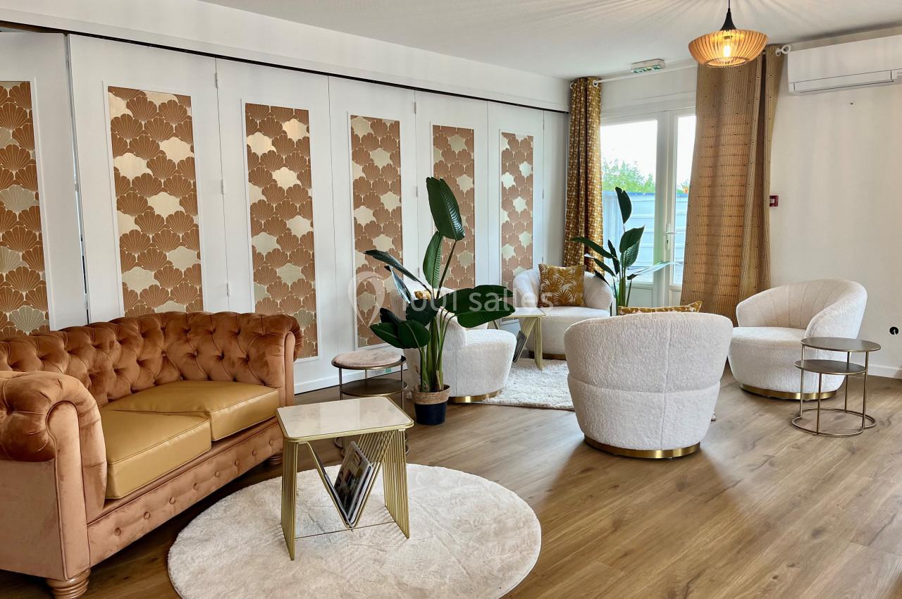 Salon lumineux avec canapé en cuir, fauteuils blancs, plantes vertes et table basse sur un parquet en bois.