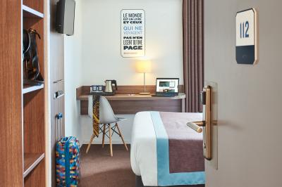 Chambre d'hôtel avec lit double, bureau équipé, lampe allumée et fenêtre avec rideaux marron.