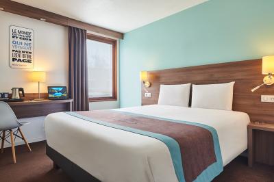 Chambre d'hôtel avec lit double, bureau équipé, lampe allumée et fenêtre avec rideaux marron.