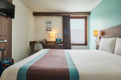 Chambre d'hôtel avec lit double, bureau équipé, lampe allumée et fenêtre avec rideaux marron.