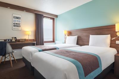 Chambre d'hôtel avec lit double, bureau équipé, lampe allumée et fenêtre avec rideaux marron.