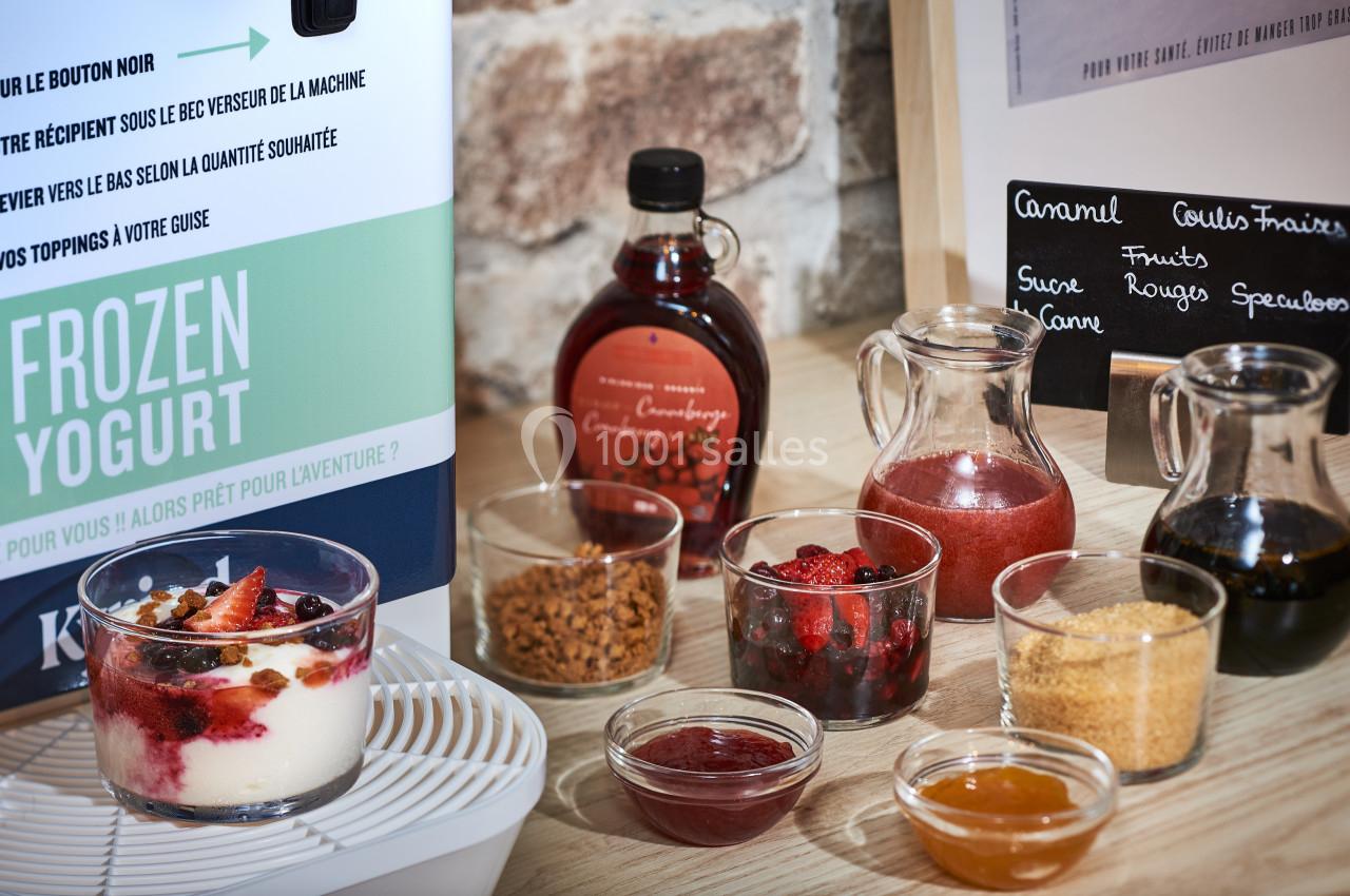 Bar à toppings pour yaourt glacé avec fruits rouges, sirops, caramel, spéculoos et sucre, présenté sur une table.