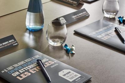 Chambre d'hôtel avec lit double, bureau équipé, lampe allumée et fenêtre avec rideaux marron.