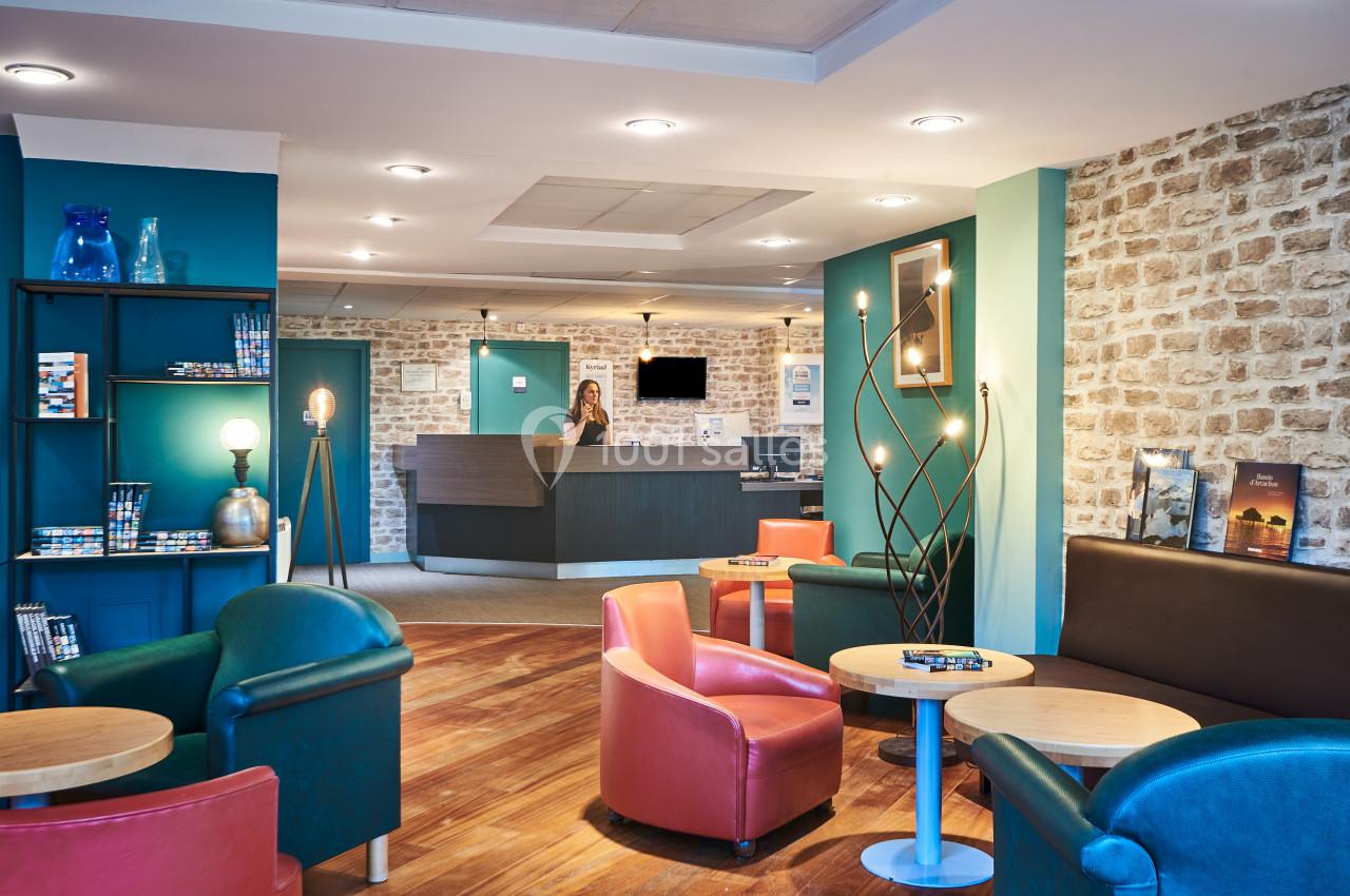 Espace d'accueil lumineux avec comptoir de réception, fauteuils colorés, tables basses et murs en pierre apparente.