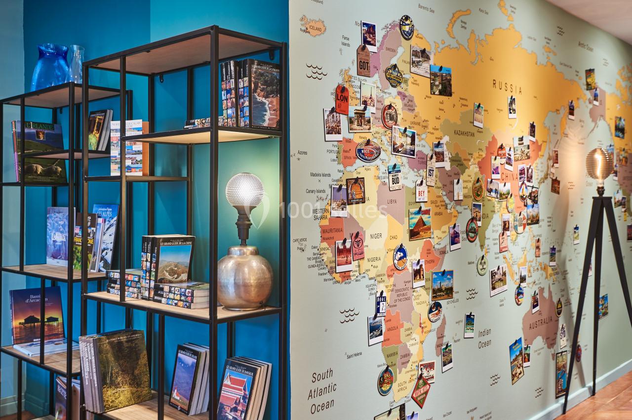 Carte du monde décorative sur un mur, entourée d'étagères contenant des livres et des objets divers.