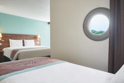 Chambre d'hôtel avec lit double, bureau équipé, lampe allumée et fenêtre avec rideaux marron.