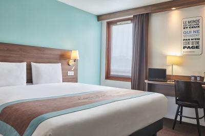 Chambre d'hôtel avec lit double, bureau équipé, lampe allumée et fenêtre avec rideaux marron.