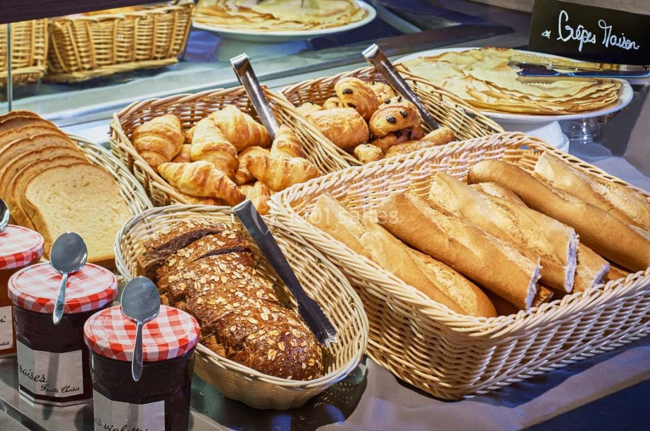 Assortiment de pains, viennoiseries et confitures disposés sur un buffet de petit-déjeuner.