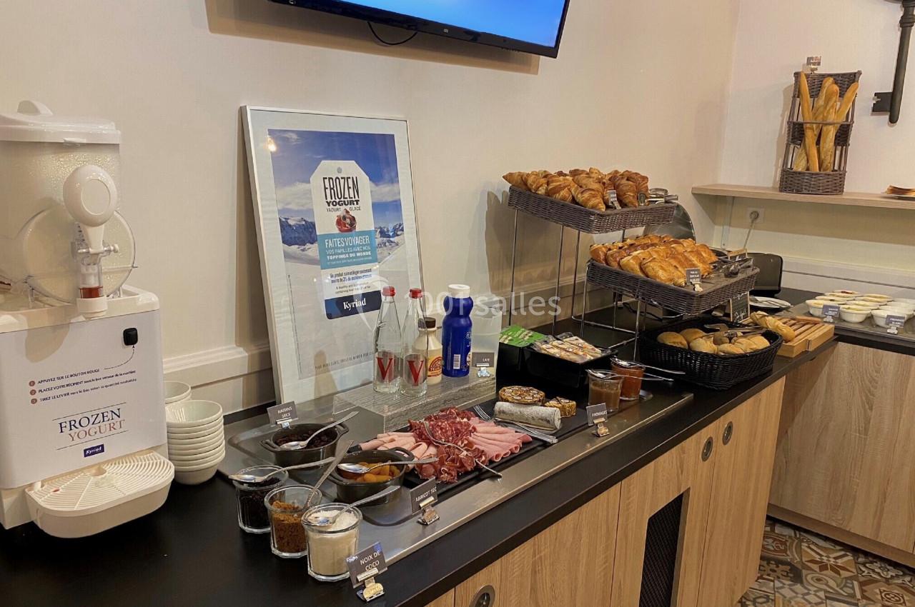 Buffet de petit-déjeuner avec viennoiseries, charcuterie, yaourt, boissons et condiments sur un comptoir en bois.