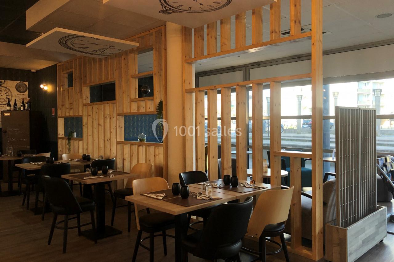 Salle de restaurant moderne avec tables dressées, chaises variées et cloisons en bois laissant passer la lumière.