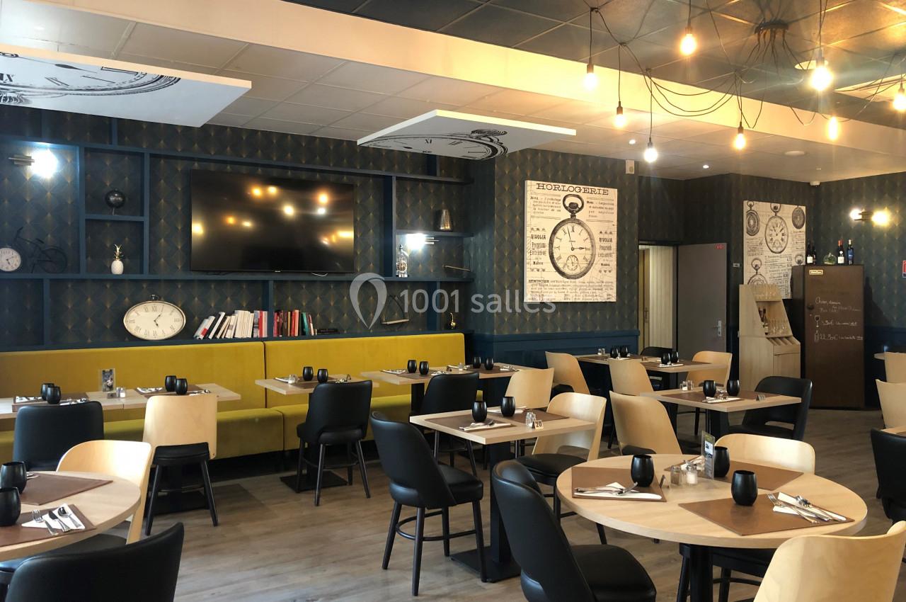 Salle de restaurant moderne avec tables dressées, chaises en bois et banquettes, éclairage suspendu et décoration murale.