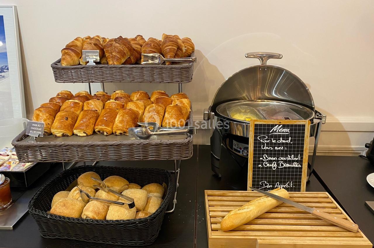 Buffet avec viennoiseries, pains variés dans des paniers et une marmite contenant des œufs brouillés.
