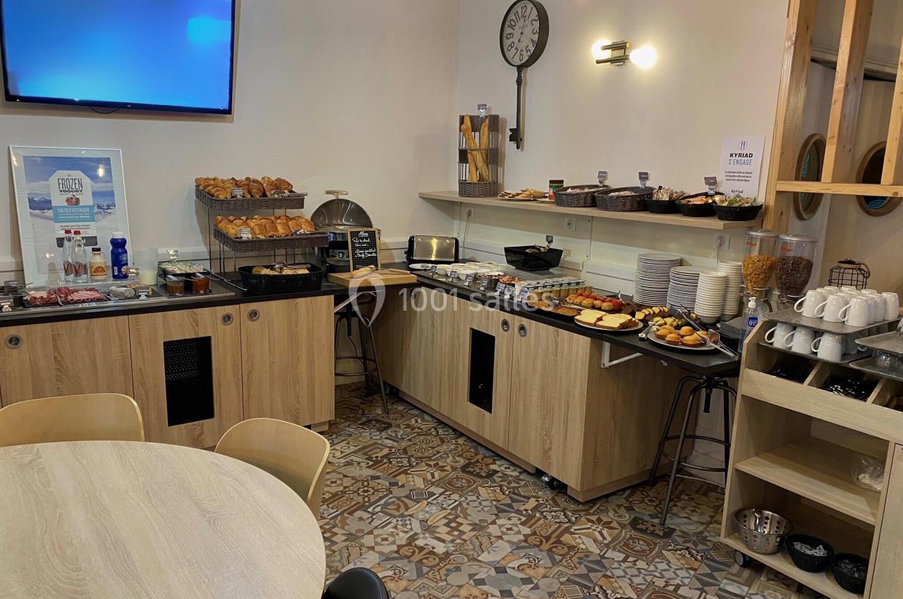 Buffet de petit-déjeuner avec viennoiseries, pains, céréales, boissons chaudes et assiettes disposés sur des meubles en bois.