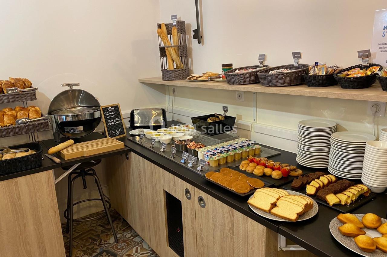 Buffet de petit-déjeuner avec pains, viennoiseries, yaourts, fruits, confitures et boissons disposés sur un comptoir.
