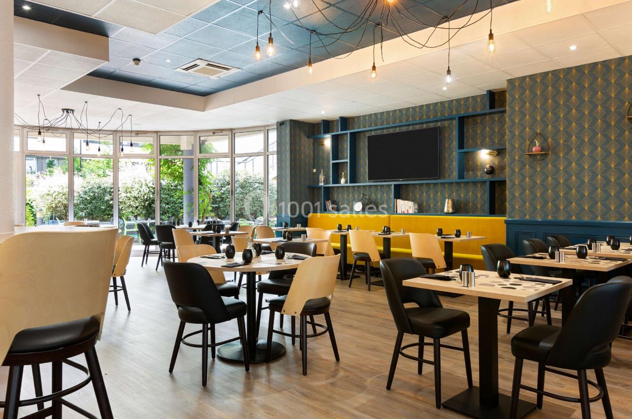 Salle de restaurant moderne avec tables dressées, chaises noires et décoration murale géométrique dans des tons bleus et…