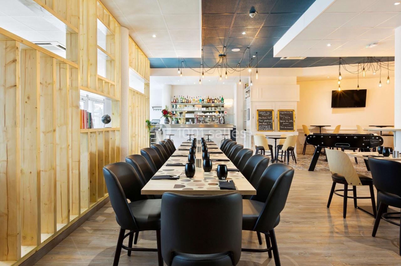 Salle de restaurant moderne avec tables dressées, bar en arrière-plan et baby-foot dans un coin.