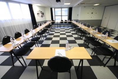 Salle de réunion avec tables disposées en U, bouteilles d'eau, stylos et blocs-notes sur chaque place.