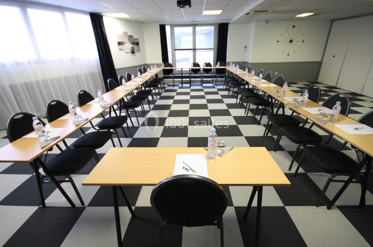 Salle de réunion lumineuse avec tables disposées en U, chaises noires et bouteilles d'eau sur chaque table.