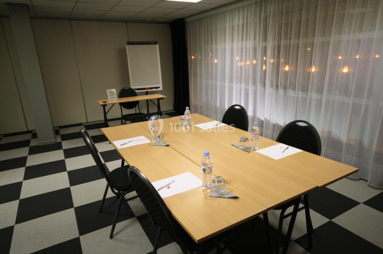 Salle de réunion avec tables disposées en rectangle, chaises noires, bloc-notes, bouteilles d'eau et paperboard en arrière…