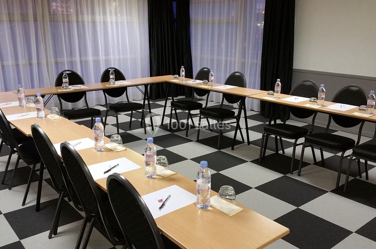 Salle de réunion avec tables disposées en U, chaises alignées, bouteilles d'eau, blocs-notes et stylos sur chaque place.