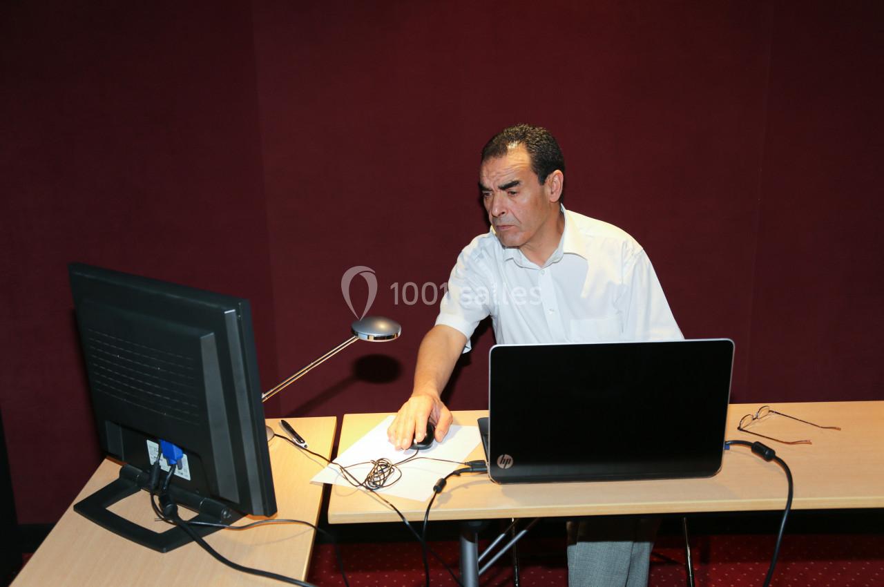 Un homme assis à un bureau utilise un ordinateur portable et un écran externe dans une pièce aux murs rouges.