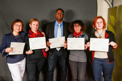 Un groupe de personnes pose devant une bannière, une femme au centre tient un diplôme.
