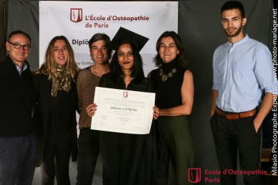 Un groupe de personnes pose devant une bannière, une femme au centre tient un diplôme.