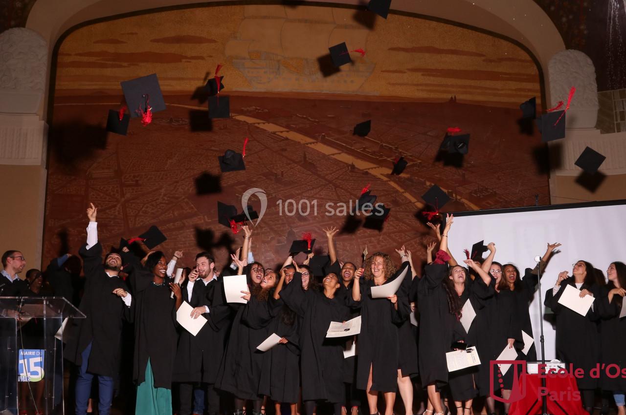Des étudiants en toges noires célèbrent leur remise de diplômes en lançant leurs mortiers en l'air dans une salle décorée.