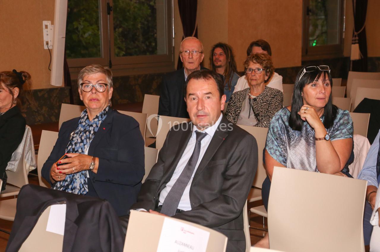 Des personnes assises dans une salle de conférence, regardant vers l'avant, avec des fenêtres en arrière-plan.