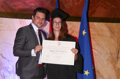 Un groupe de personnes pose devant une bannière, une femme au centre tient un diplôme.