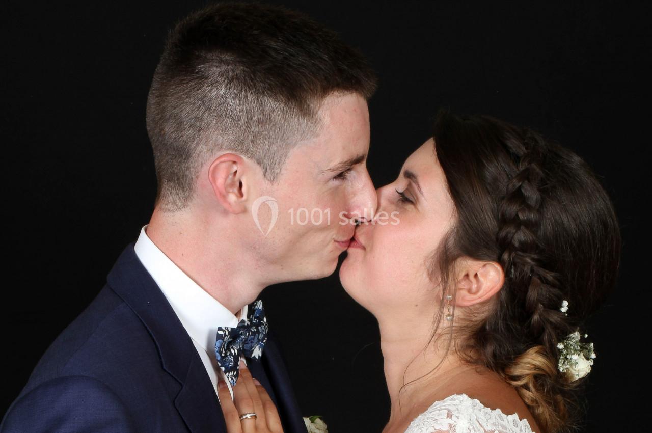 Un couple s'embrasse tendrement, vêtu d'une tenue de mariage, sur un fond noir.