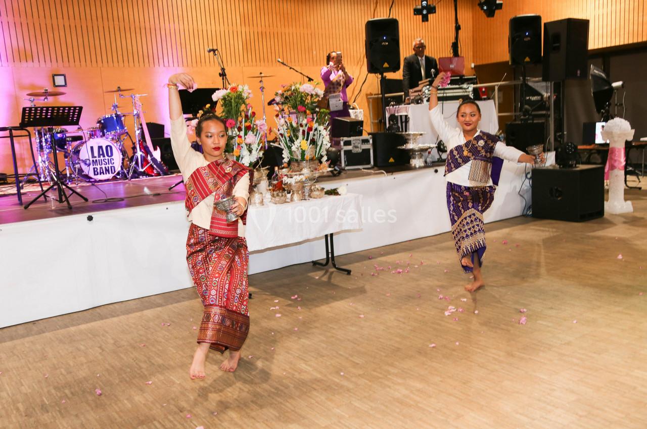 Des danseuses en tenue traditionnelle exécutent une chorégraphie devant une scène avec des musiciens et des décorations.