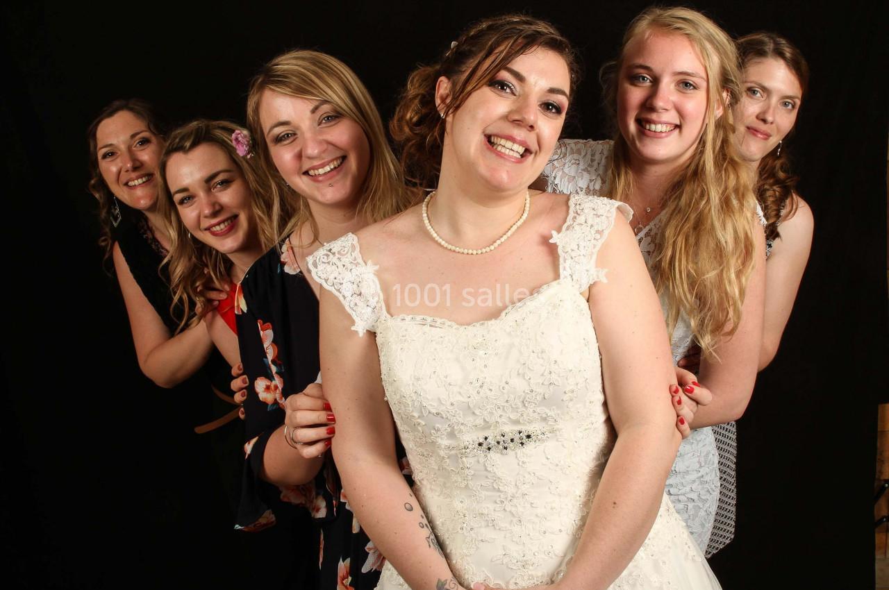 Un groupe de femmes souriantes, dont une en robe de mariée, posant devant un fond noir.