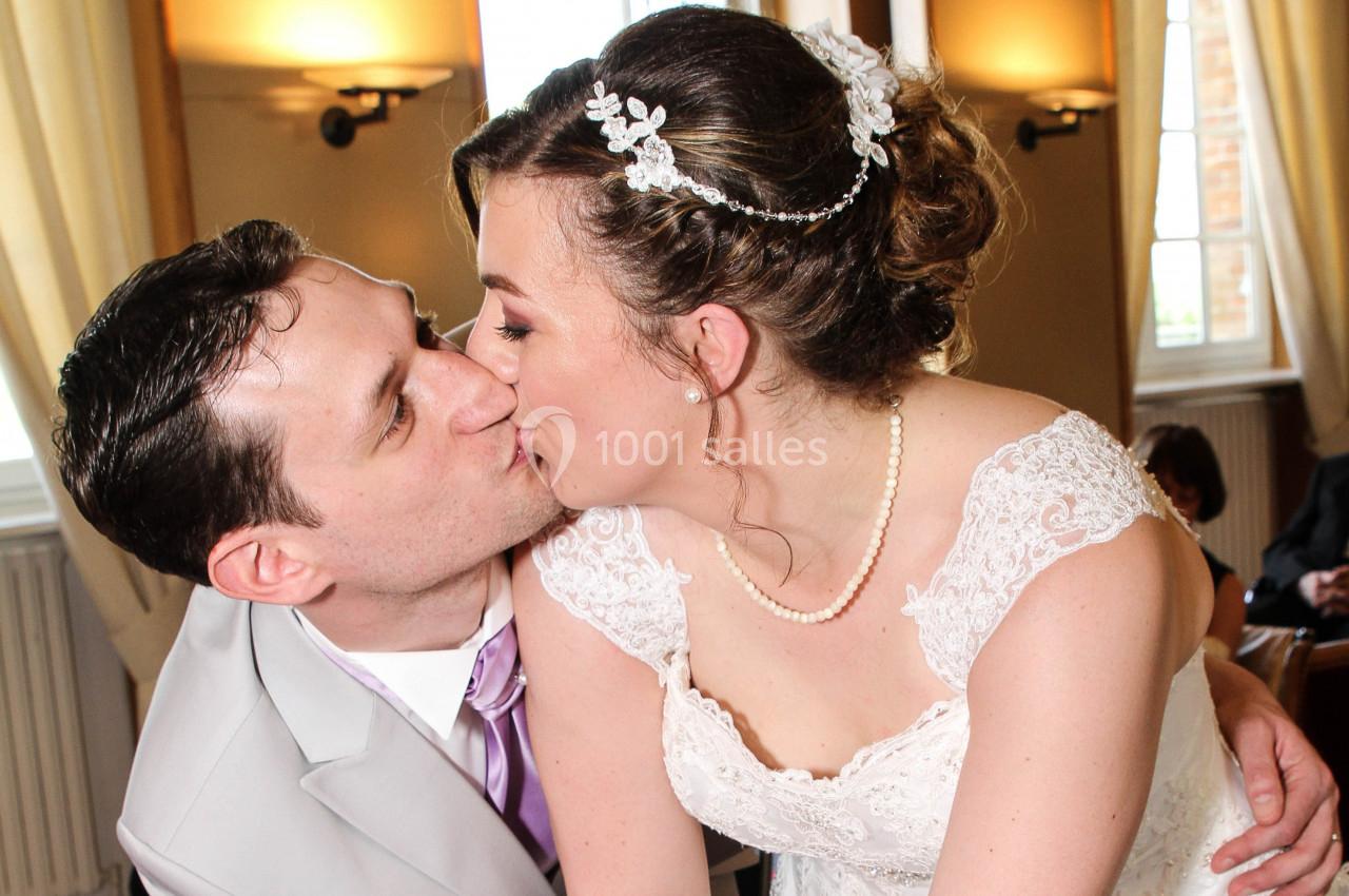 Un couple de mariés s'embrassant dans une salle éclairée par la lumière naturelle des fenêtres.