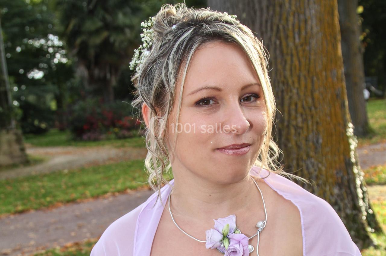 Femme souriante en tenue élégante avec des fleurs dans les cheveux, posant dans un parc verdoyant.