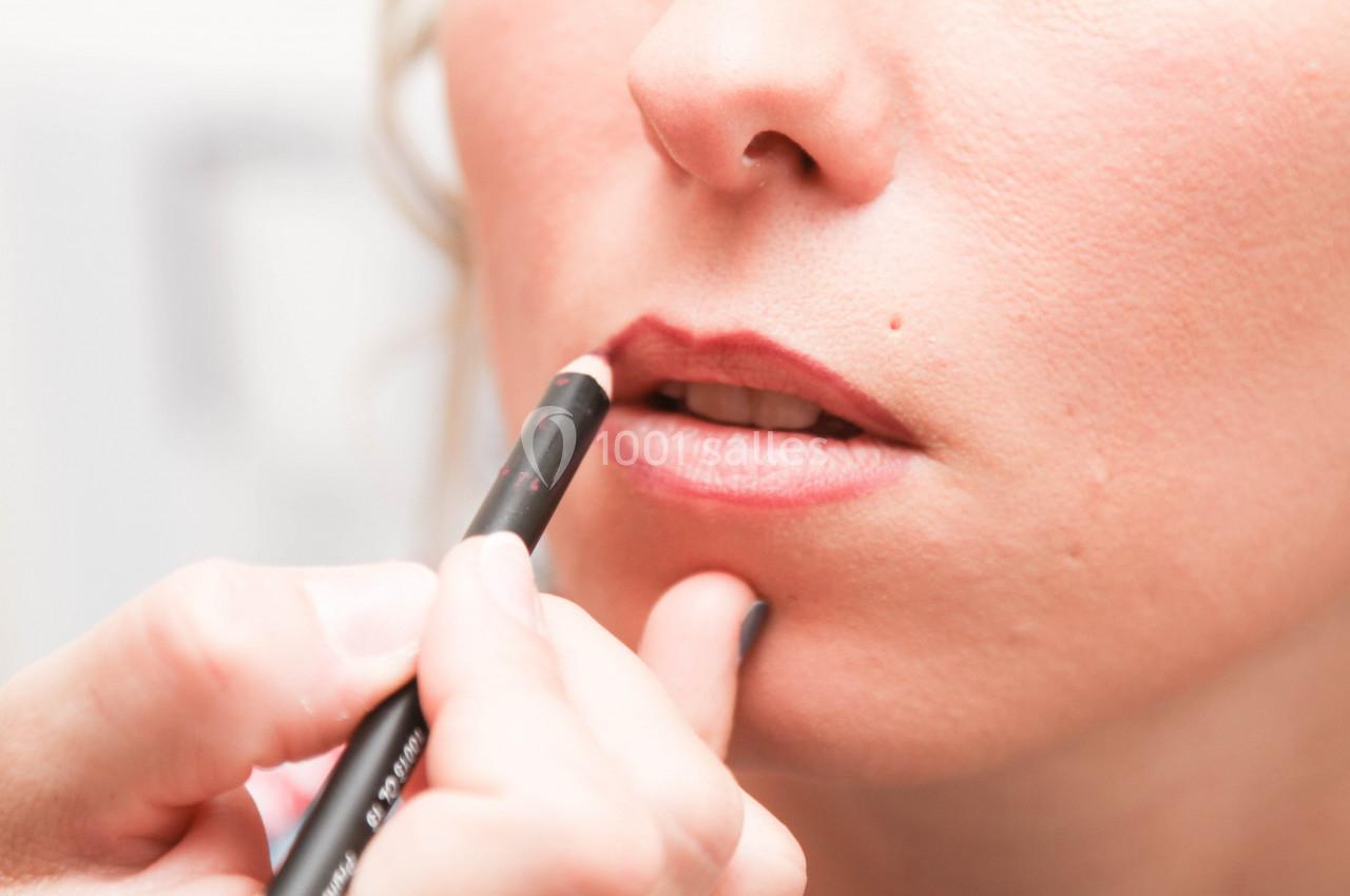 Application de crayon à lèvres sur les contours de la bouche d'une femme par une main visible.