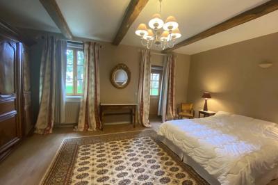 Vase de pivoines roses sur une table en bois, entouré de livres, chandeliers et fauteuils dans un salon élégant.