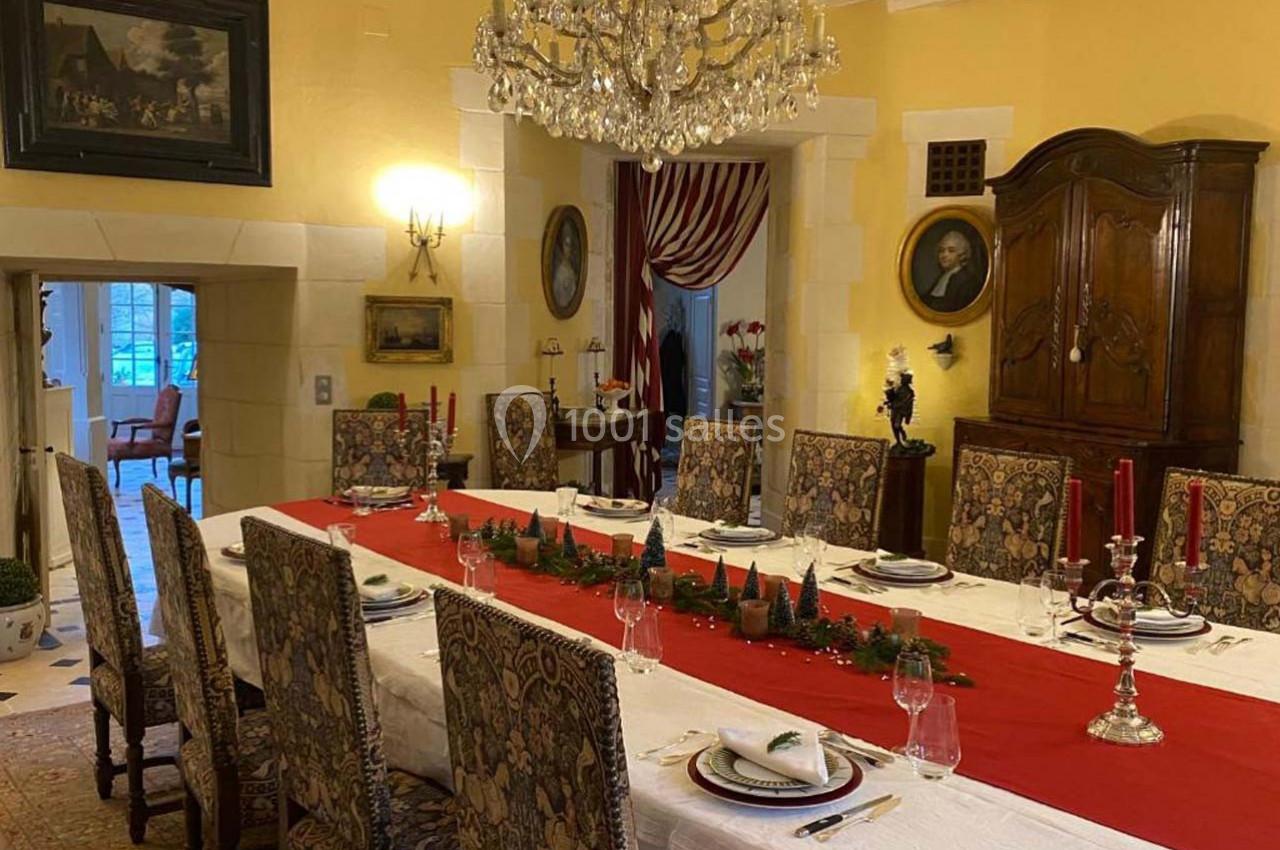 Salle à manger élégante avec une grande table dressée, nappe blanche, chemin de table rouge et chandeliers.