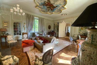 Vase de pivoines roses sur une table en bois, entouré de livres, chandeliers et fauteuils dans un salon élégant.