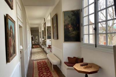 Vase de pivoines roses sur une table en bois, entouré de livres, chandeliers et fauteuils dans un salon élégant.