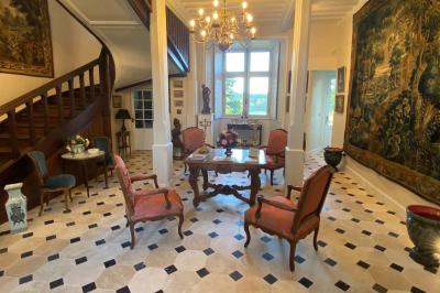 Vase de pivoines roses sur une table en bois, entouré de livres, chandeliers et fauteuils dans un salon élégant.